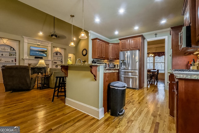 kitchen featuring a kitchen breakfast bar, light wood-style floors, appliances with stainless steel finishes, a peninsula, and light stone countertops