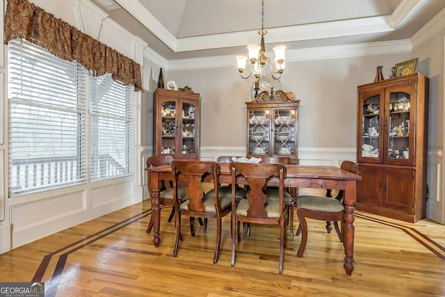 dining room featuring crown molding, a chandelier, wainscoting, light wood-style floors, and a raised ceiling