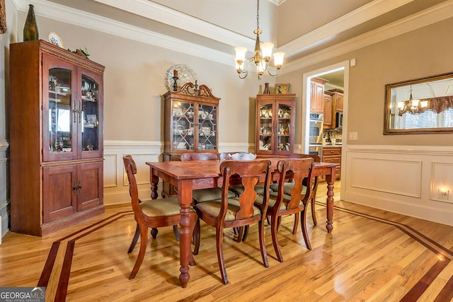 dining area with an inviting chandelier, light wood-style flooring, and a wainscoted wall