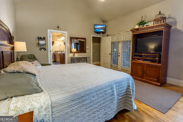 bedroom featuring ensuite bath, wood finished floors, baseboards, and high vaulted ceiling