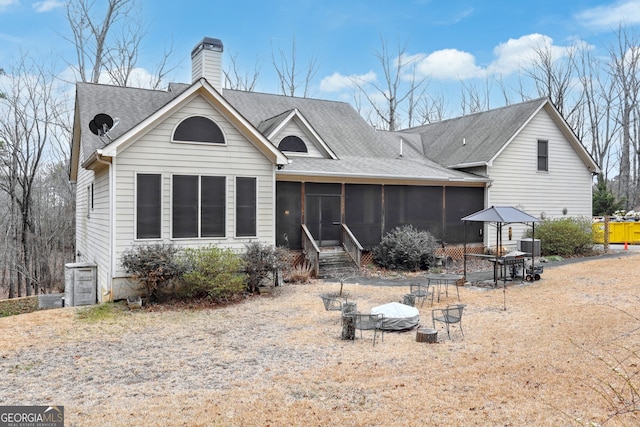 back of property with central AC, a fire pit, roof with shingles, a sunroom, and a chimney