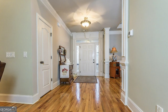 foyer entrance with crown molding, light wood-type flooring, baseboards, and decorative columns