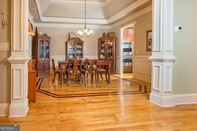 dining space with a notable chandelier, decorative columns, a raised ceiling, and light wood finished floors