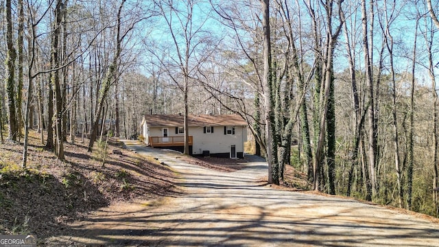 view of front facade featuring a view of trees, driveway, and a wooden deck