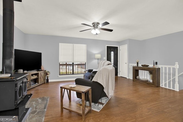 living area with a wood stove, wood finished floors, baseboards, and ceiling fan