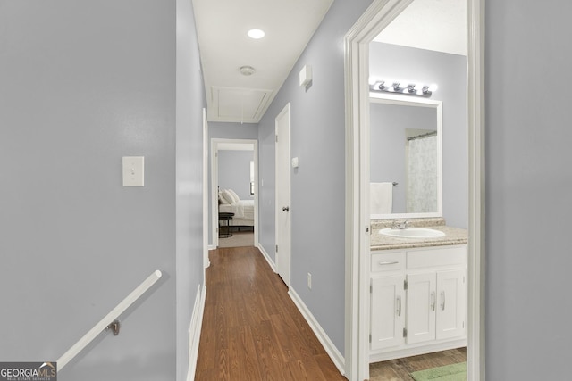 hall with baseboards, attic access, dark wood-style flooring, a sink, and an upstairs landing