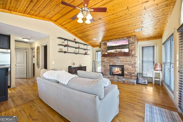 living area with visible vents, lofted ceiling, a stone fireplace, and light wood-style flooring