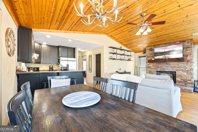 dining room featuring wood ceiling, vaulted ceiling, ceiling fan with notable chandelier, a fireplace, and wood finished floors