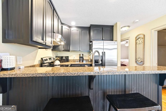 kitchen with a textured ceiling, appliances with stainless steel finishes, a peninsula, and extractor fan