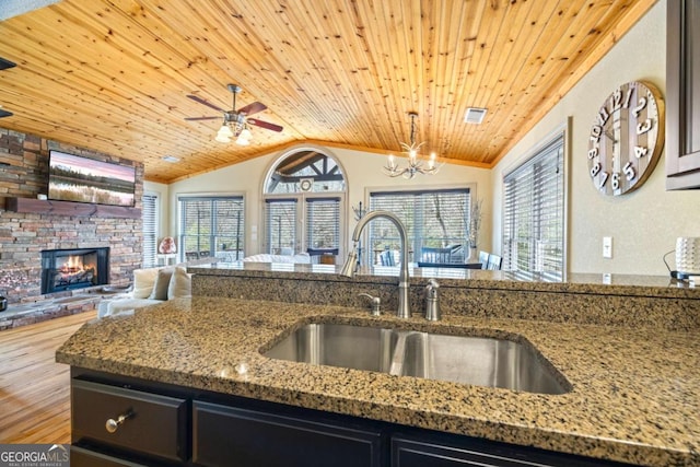 kitchen featuring wood ceiling, lofted ceiling, light stone counters, a stone fireplace, and a sink