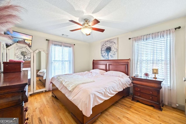 bedroom with visible vents, light wood-style floors, a ceiling fan, and a textured ceiling