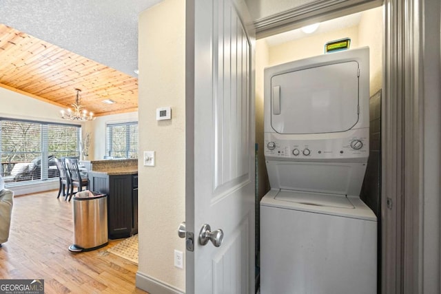 washroom featuring light wood-style floors, wooden ceiling, stacked washer / dryer, a chandelier, and laundry area