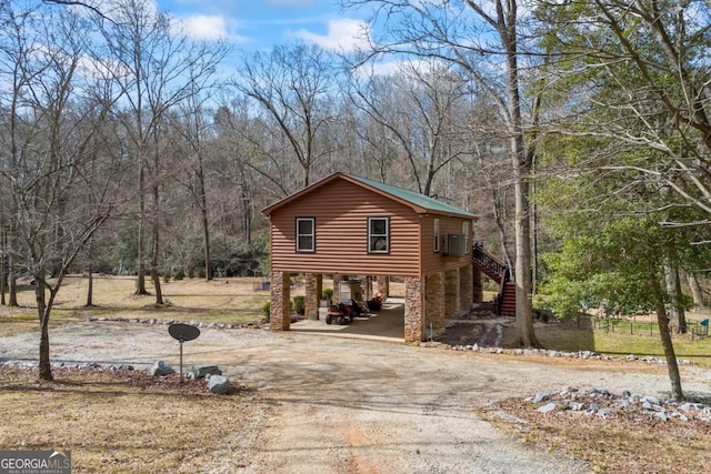 view of side of home featuring stairway, cooling unit, a carport, dirt driveway, and faux log siding