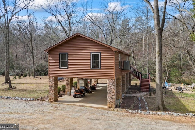 view of home's exterior featuring stairway, dirt driveway, central AC, and faux log siding