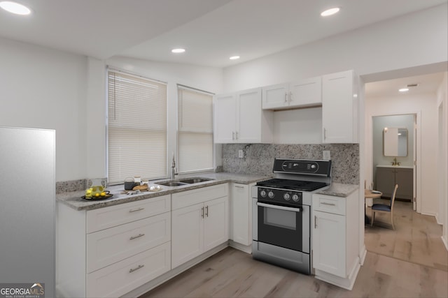 kitchen featuring light wood-style flooring, a sink, gas range oven, white cabinetry, and backsplash