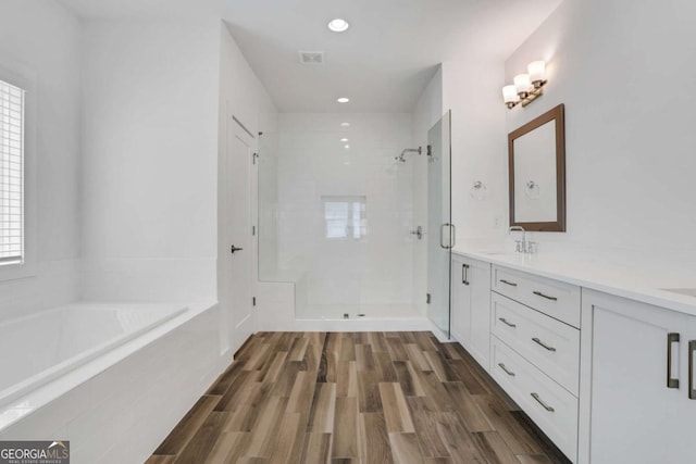 full bath featuring a sink, wood finished floors, a shower stall, double vanity, and a bath