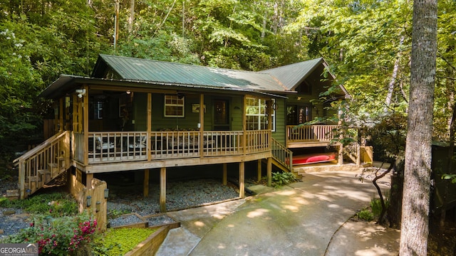 view of front of property featuring stairway, a view of trees, covered porch, and metal roof