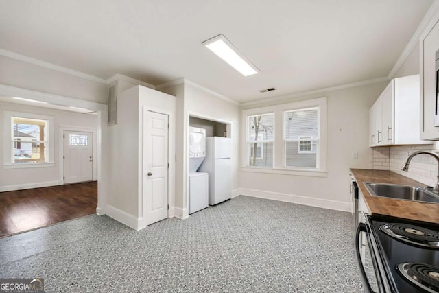 kitchen with stacked washer / dryer, a sink, baseboards, butcher block counters, and white cabinetry