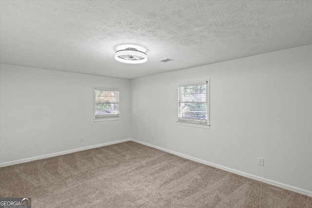 carpeted spare room featuring visible vents, baseboards, and a textured ceiling