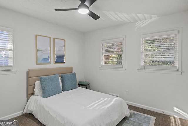 bedroom featuring baseboards, multiple windows, ceiling fan, and dark carpet
