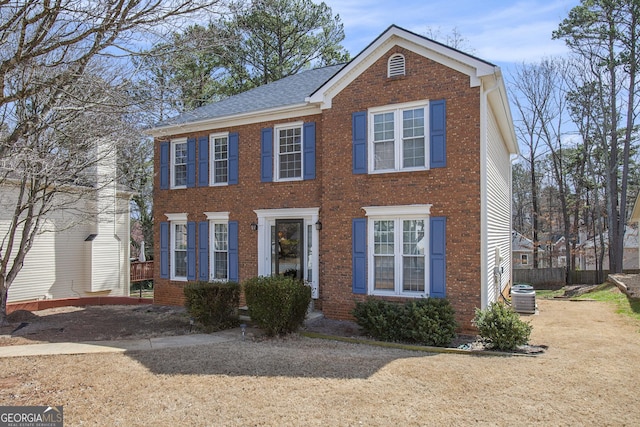 colonial inspired home featuring central air condition unit, brick siding, and a shingled roof