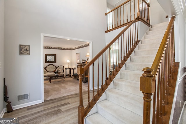 staircase with a high ceiling, wood finished floors, visible vents, and baseboards