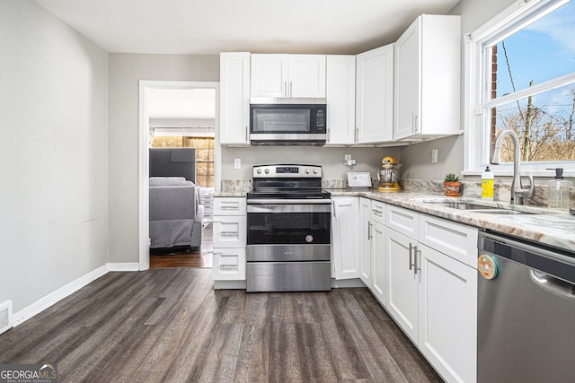 kitchen with light stone countertops, dark wood finished floors, a sink, white cabinets, and appliances with stainless steel finishes