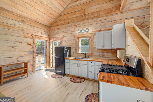 kitchen featuring butcher block countertops, a sink, freestanding refrigerator, gas range, and a healthy amount of sunlight