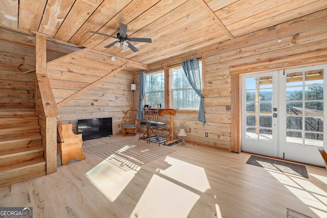 unfurnished living room featuring wooden walls, wooden ceiling, a fireplace, french doors, and wood finished floors