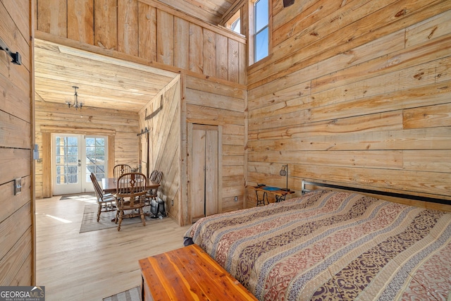 bedroom featuring wooden walls, wood finished floors, a towering ceiling, and access to exterior