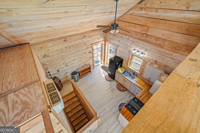 unfurnished living room with a sink, wood finished floors, wooden walls, ceiling fan, and vaulted ceiling