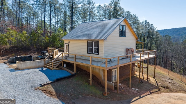 rear view of property featuring a deck, a forest view, and metal roof