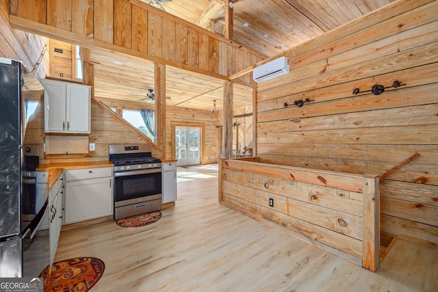 kitchen featuring stainless steel range with gas stovetop, wood walls, wood ceiling, a wall unit AC, and white cabinets