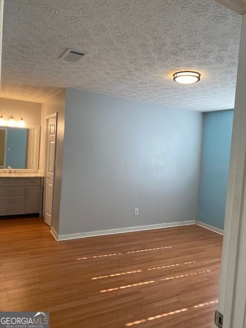 empty room with a textured ceiling, wood finished floors, visible vents, and baseboards