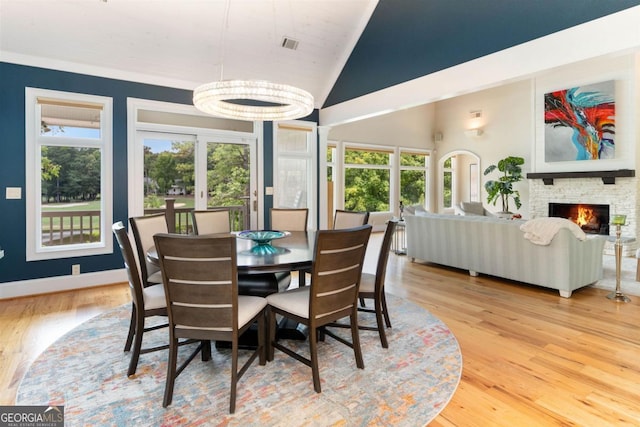 dining area featuring wood finished floors, baseboards, visible vents, high vaulted ceiling, and a fireplace