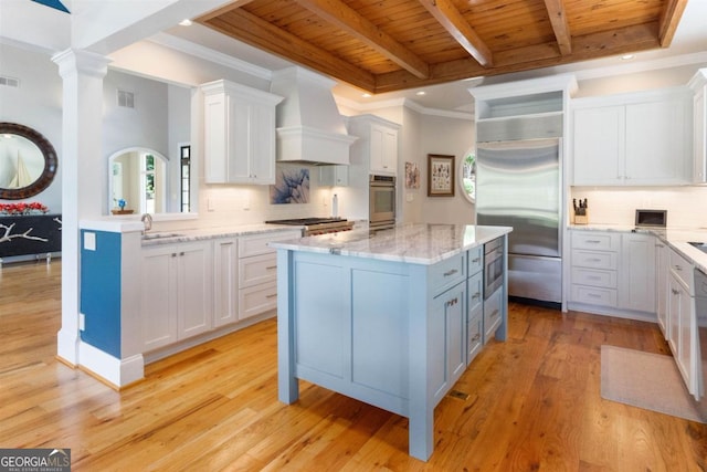 kitchen featuring built in appliances, wood ceiling, custom range hood, white cabinetry, and a sink