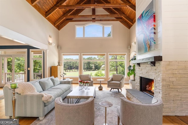 living room featuring wood finished floors, a stone fireplace, wooden ceiling, and vaulted ceiling with beams