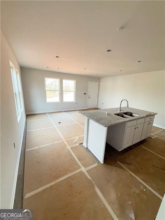 kitchen with a sink, light stone countertops, open floor plan, white cabinets, and a kitchen island with sink