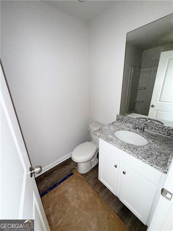 full bathroom with toilet, wood finished floors, baseboards, walk in shower, and vanity