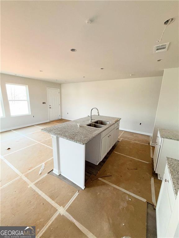 kitchen with visible vents, an island with sink, a sink, white cabinetry, and light stone countertops