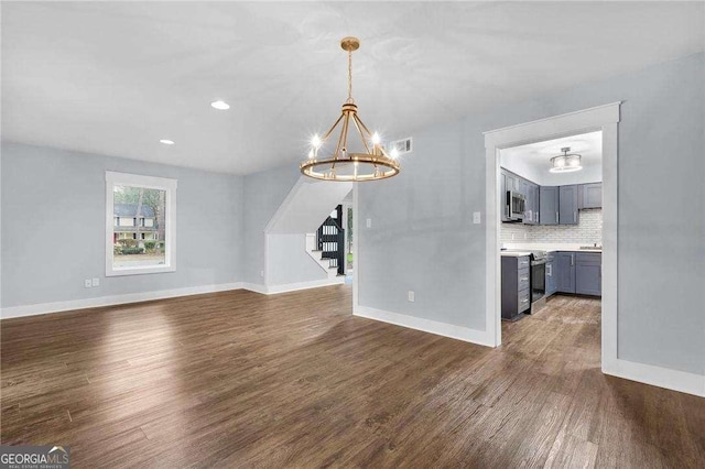 unfurnished living room featuring stairway, visible vents, baseboards, an inviting chandelier, and dark wood-style flooring