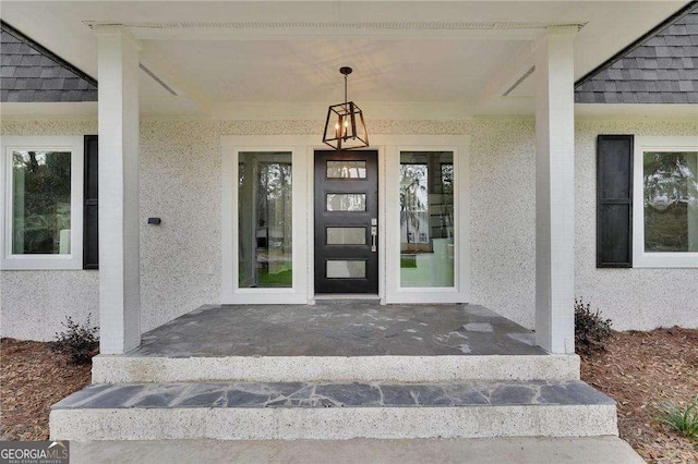 doorway to property with stucco siding, covered porch, and a shingled roof