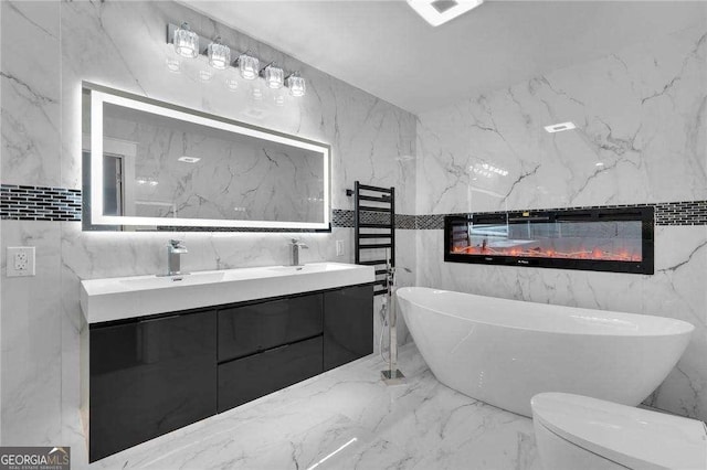 full bathroom with a glass covered fireplace, stone wall, marble finish floor, and a freestanding bath