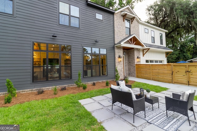 rear view of house featuring brick siding, an outdoor living space, board and batten siding, fence, and a patio