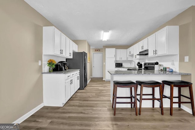 kitchen with light wood finished floors, a peninsula, electric range, freestanding refrigerator, and under cabinet range hood