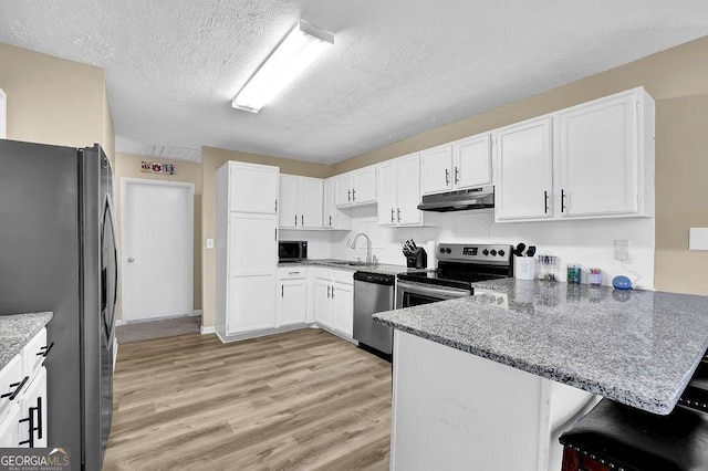 kitchen with under cabinet range hood, stone counters, light wood-style flooring, a peninsula, and stainless steel appliances