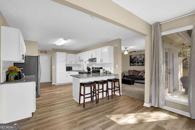 kitchen with a kitchen bar, under cabinet range hood, stainless steel appliances, light wood-style floors, and a peninsula