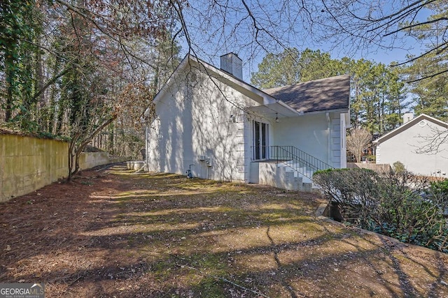 exterior space with a chimney, roof with shingles, and fence