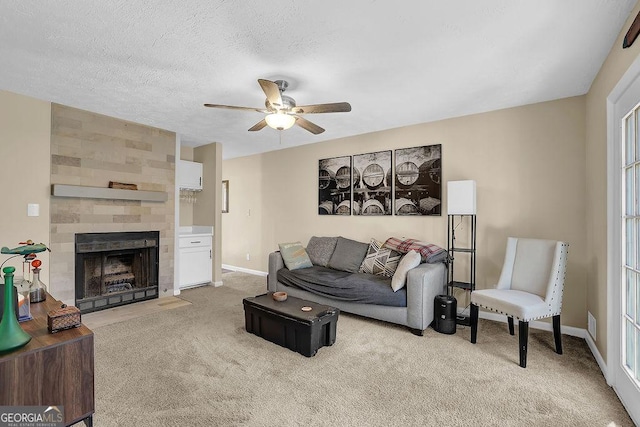 living area featuring a textured ceiling, baseboards, light colored carpet, ceiling fan, and a tile fireplace