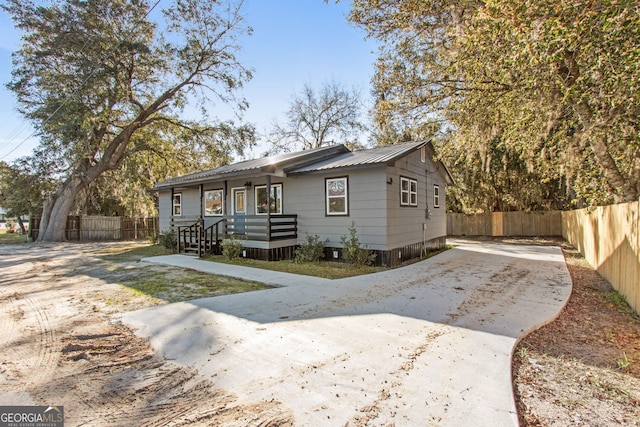 bungalow with concrete driveway, fence, and metal roof